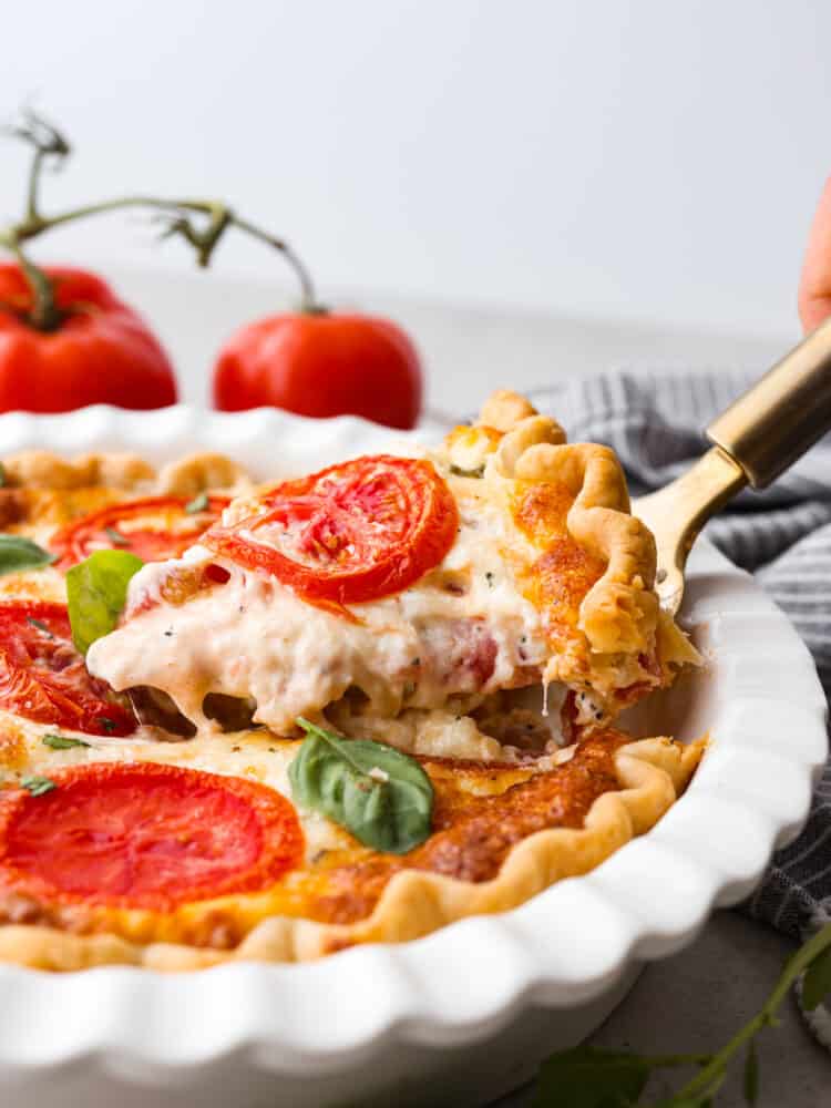 The side view of a tomato pie with a slice being taken out with a gold pie server. 