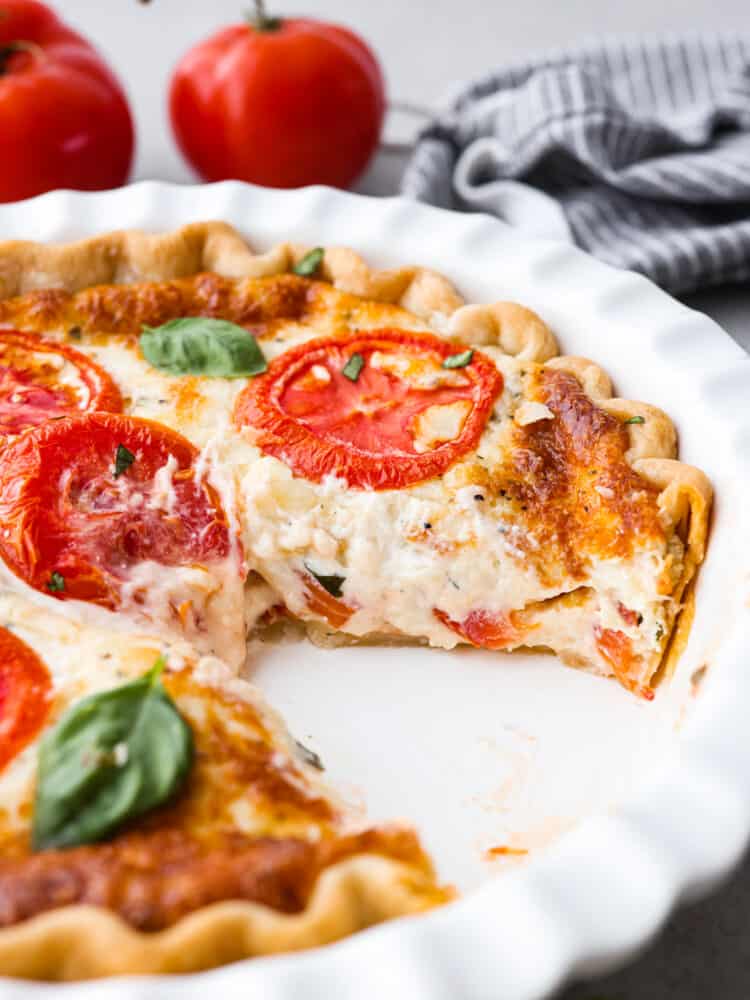 A tomato pie in a white pie pan with a slice taken out. 