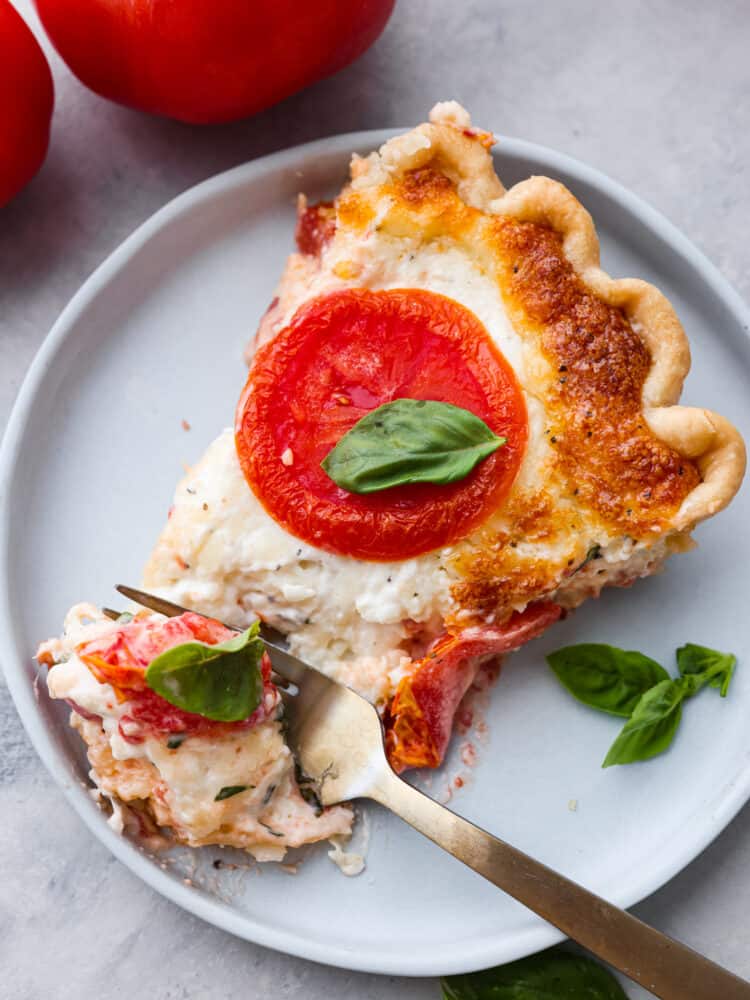 A slice of tomato pie on a plate with a gold fork. 