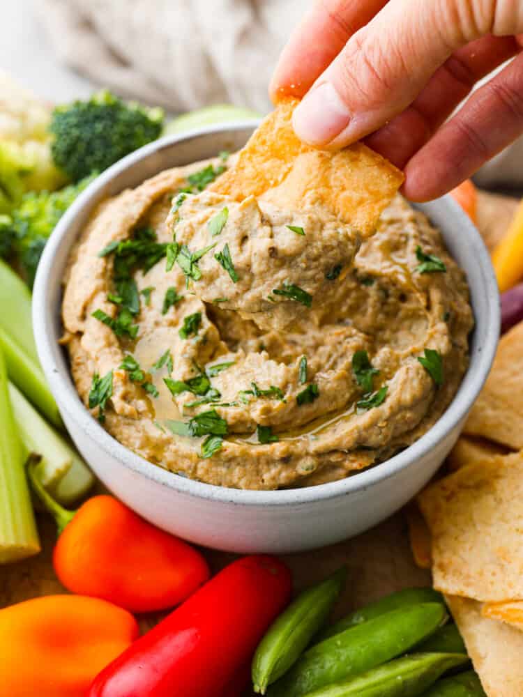 A pita chip being dipped in a bowl of baba ganoush.