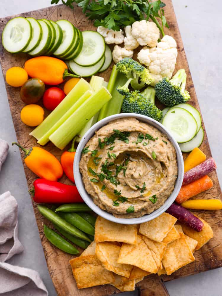 A bowl of baba ganoush dip served alongside veggies and pita chips.