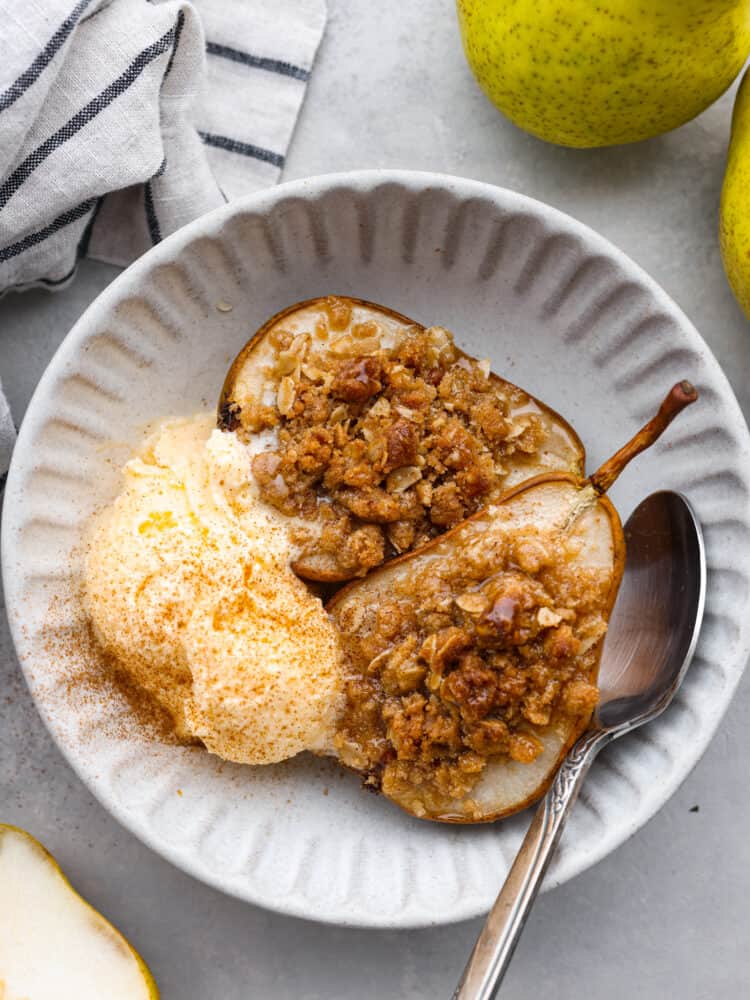 2 baked pear halves served in a white bowl with a scoop of ice cream.