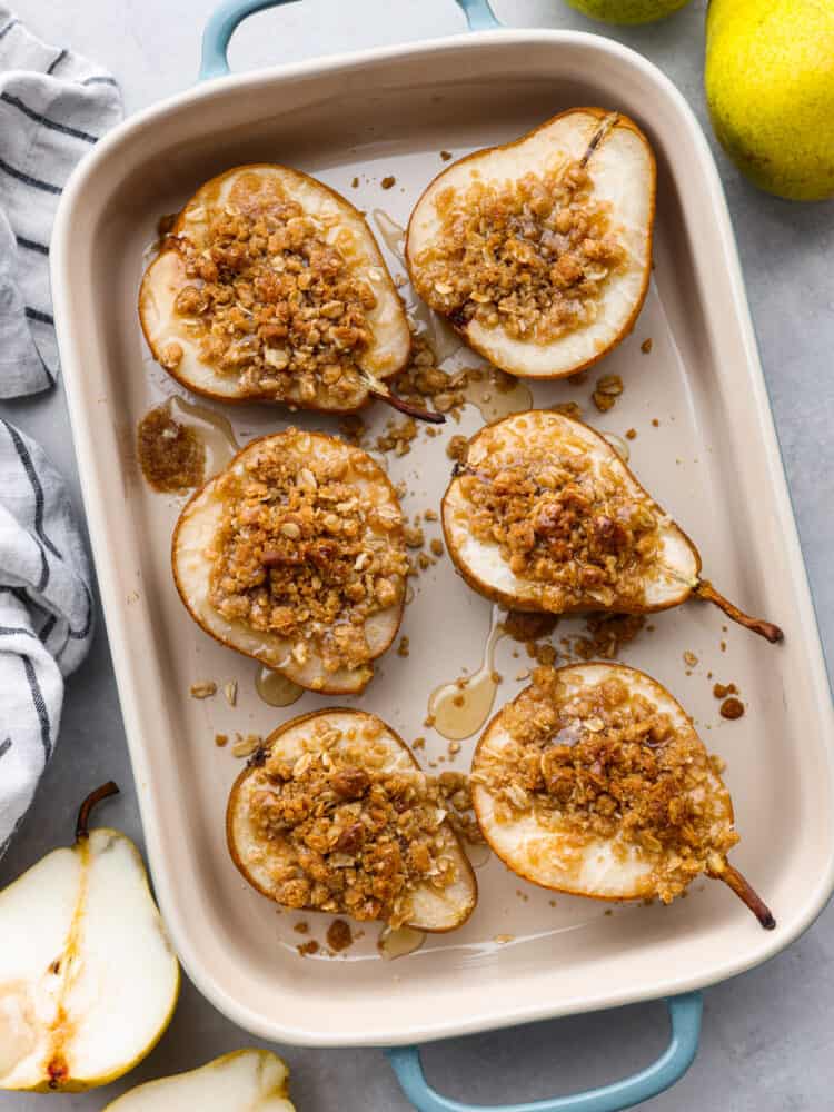 Top-down view of 6 baked pears in a metal baking dish.