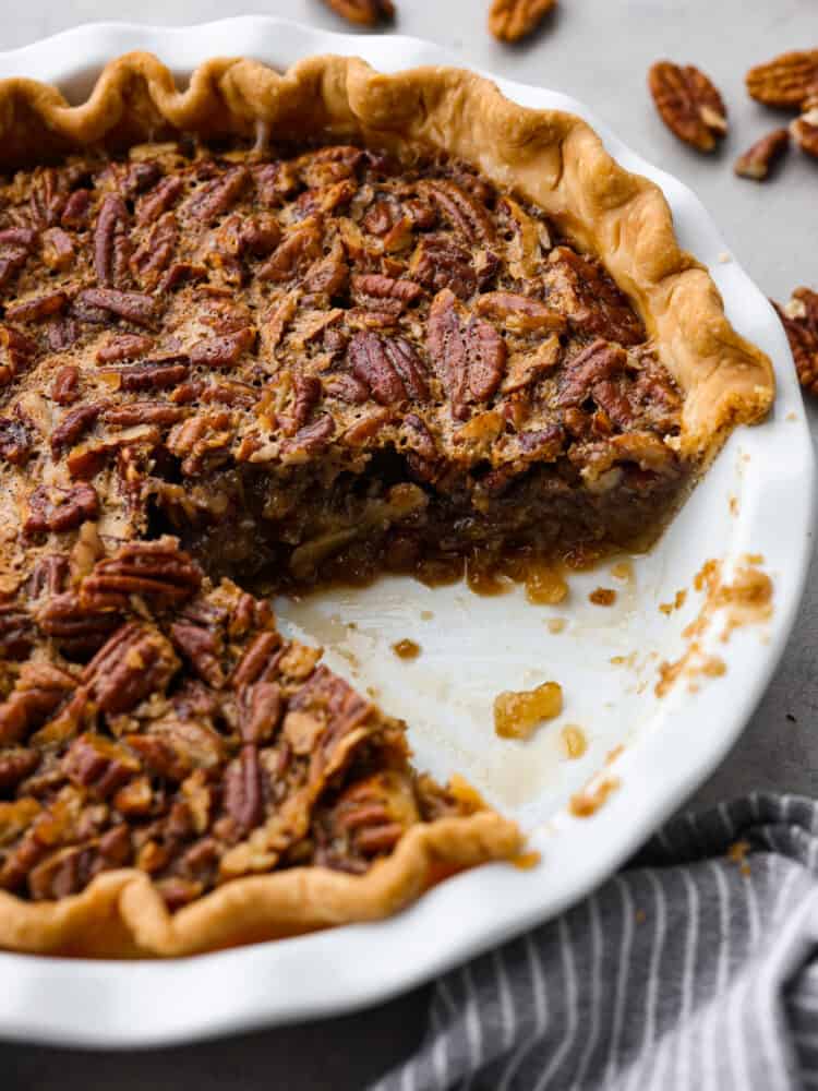 Bourbon Pecan Pie with a slice taken out of it in a white pie dish with pecans in the background.