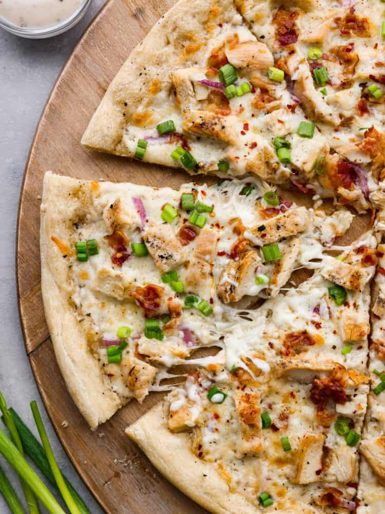 Top-down view of sliced alfredo pizza on a wooden board.