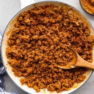 Chorizo pork in a white pan with a wooden spoon