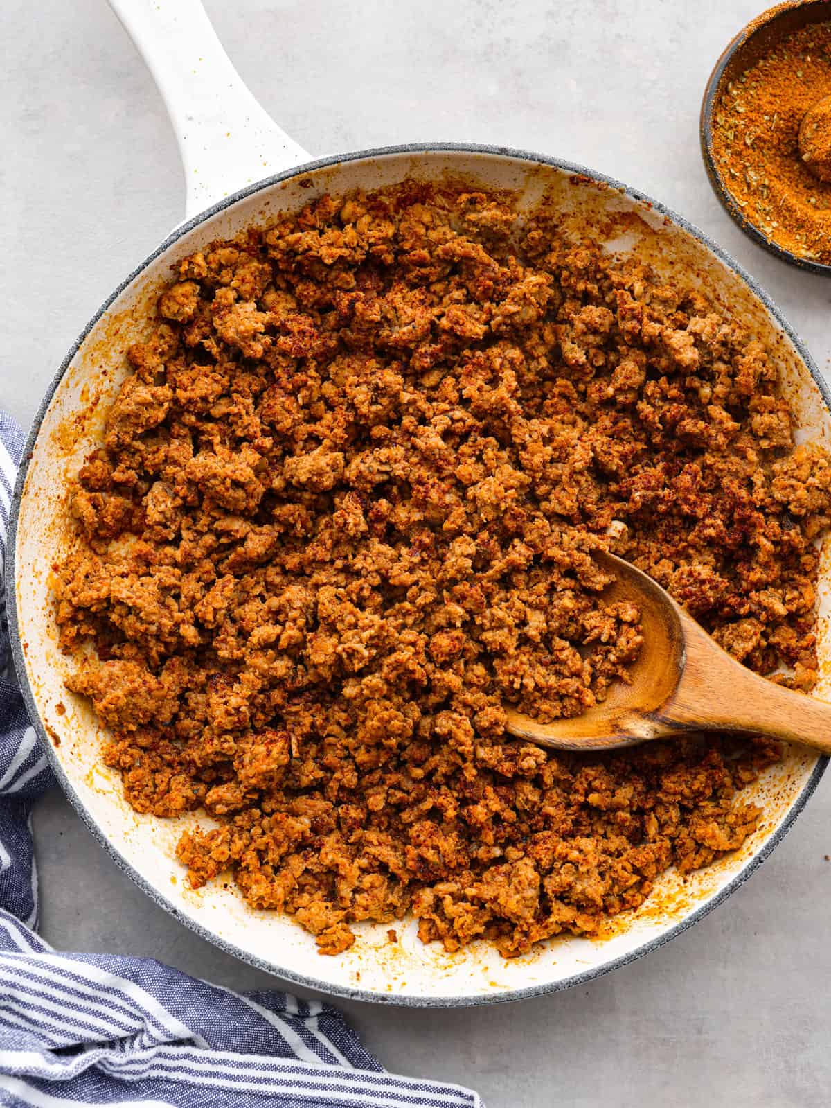 Chorizo pork in a white pan with a wooden spoon