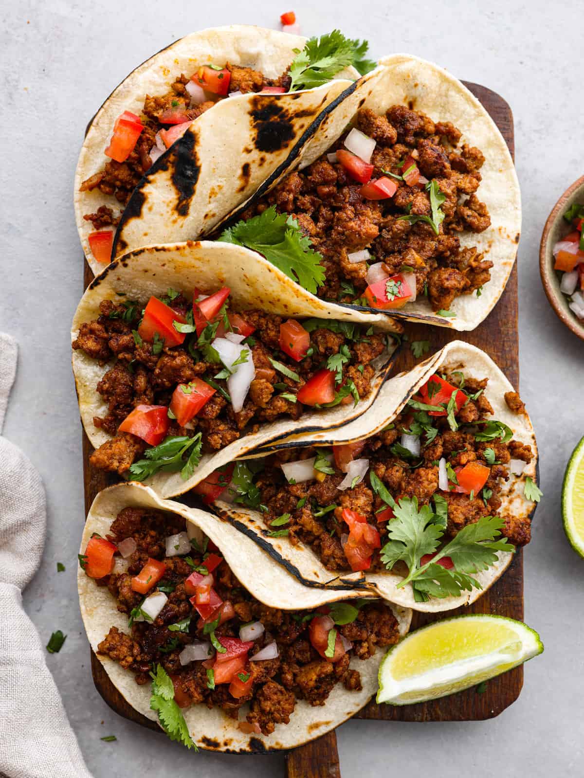 Five tacos sitting on a cutting board with limes next to them