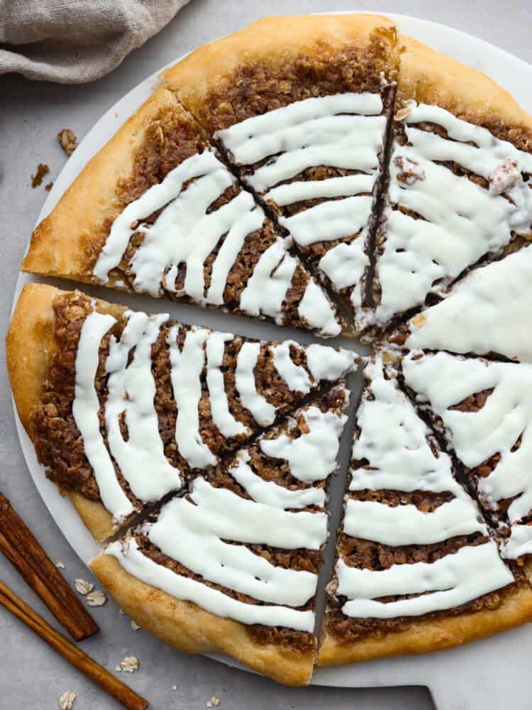 The top view of a dessert pizza, drizzled with cream cheese frosting and cut into slices on a platter. 