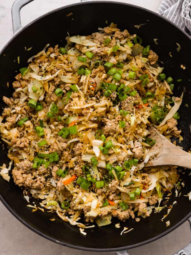 The top view of the egg roll ingredients in a pan with a wooden spoon. 