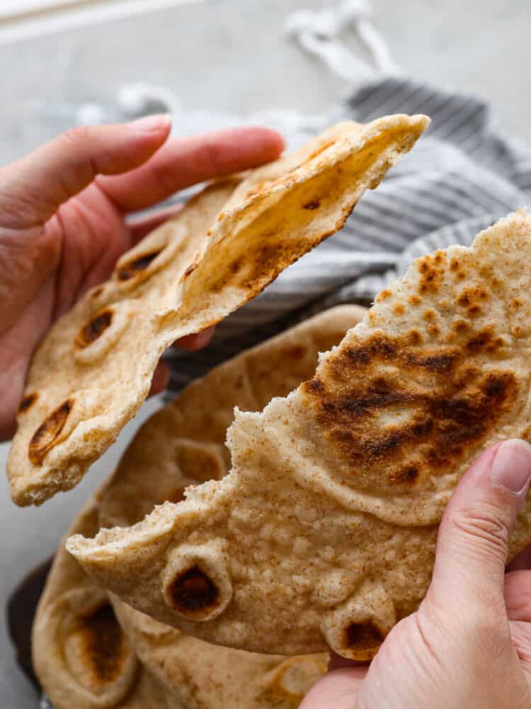 2 hands breaking a piece of pita bread apart. 