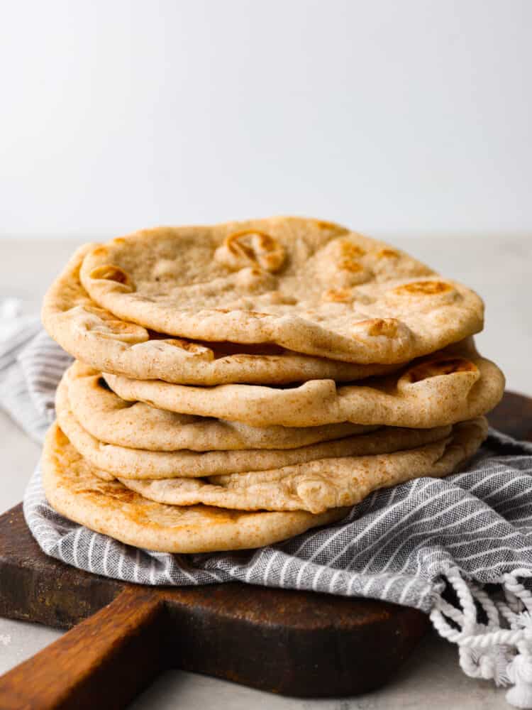 A stack of pita bread on a wooden cutting board with a blue striped tea towel. 