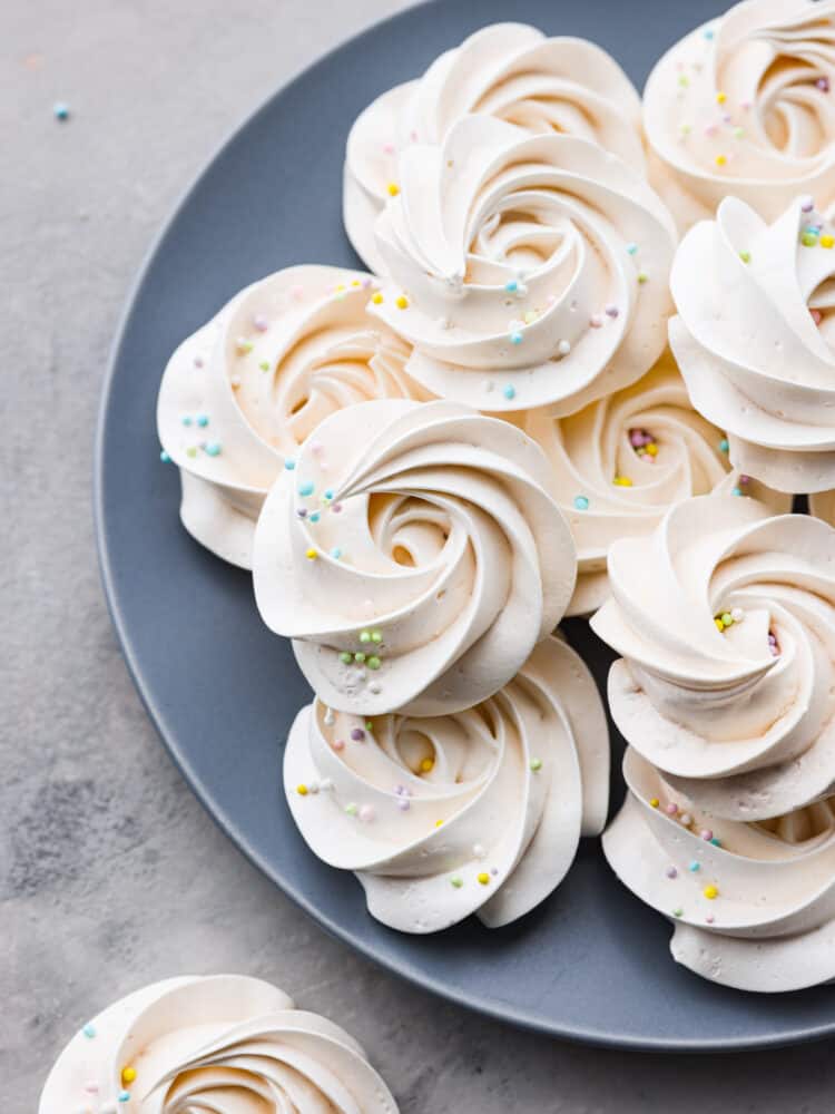 Meringue cookies sitting on a blue plate with sprinkles on top.