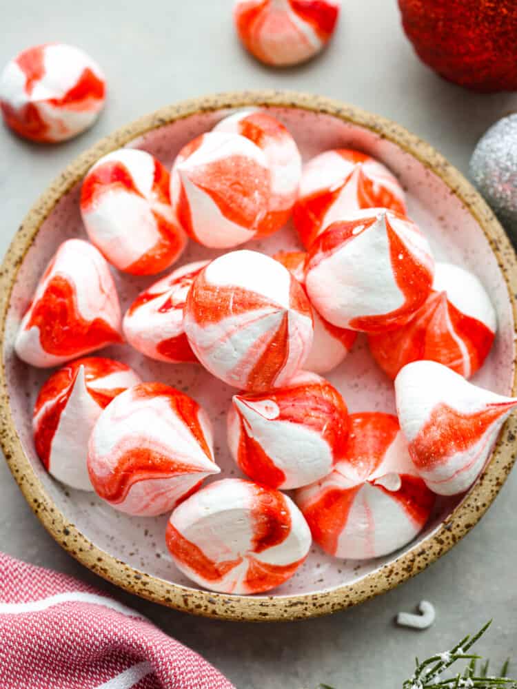 Peppermint meringue kisses in a candy dish on a table with ornaments next to it.