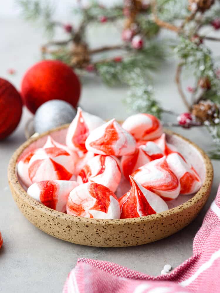 Peppermint meringue kisses in a candy dish with greenery and christmas ornaments in the background.