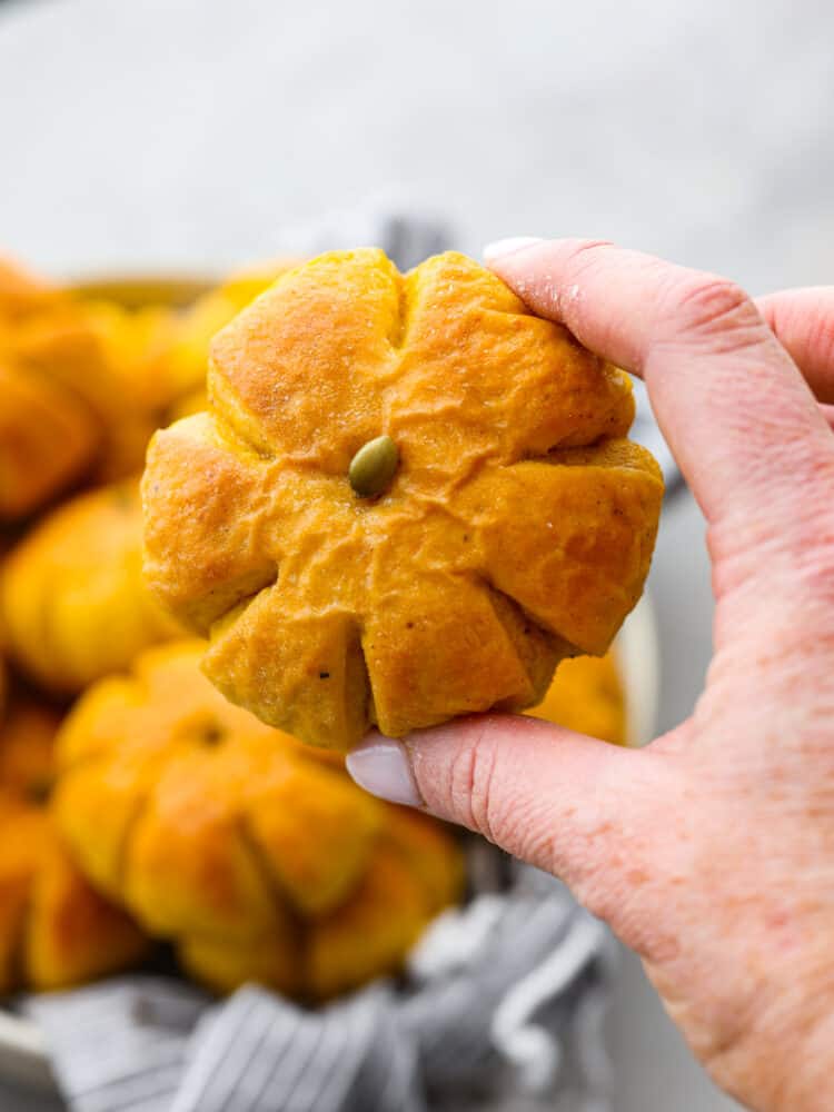 Someone holding a pumpkin dinner roll up. 