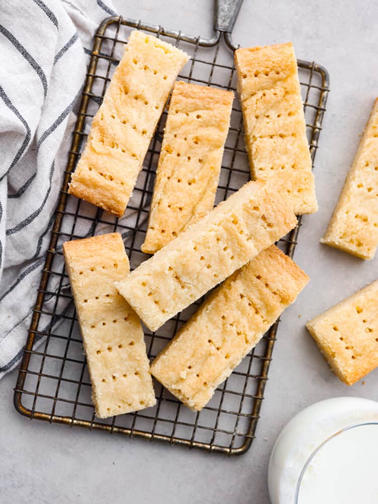 Top view of pieces of shortbread on a gray counter and a cooling rack. A glass of milk and kitchen towel are next to the cookies.