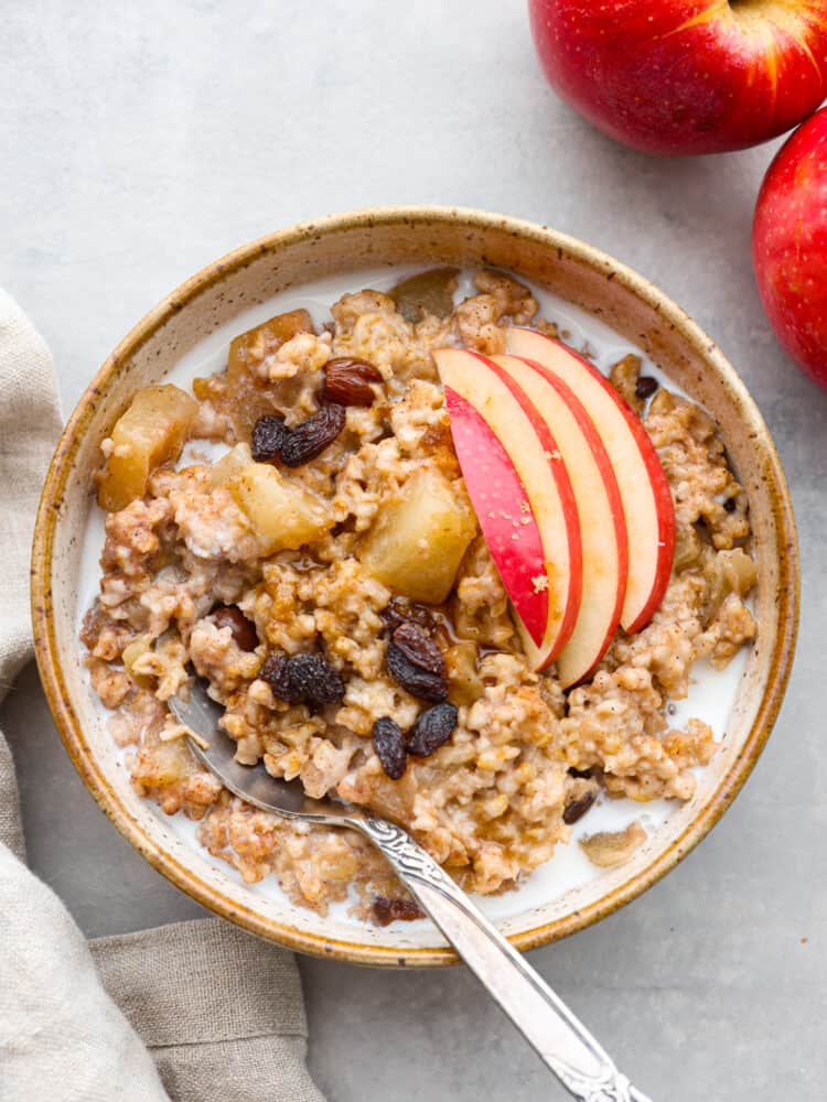 Top-down view of oatmeal served with milk and garnished with sliced apples in a stoneware bowl.