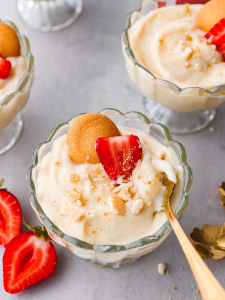 Top-down view of vanilla pudding in a glass cup being scooped with a gold spoon.