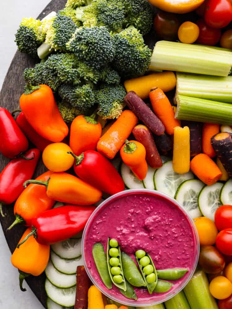 Top view of the beet hummus with sugar snap peas garnished on top.  Veggies are surrounding the hummus.