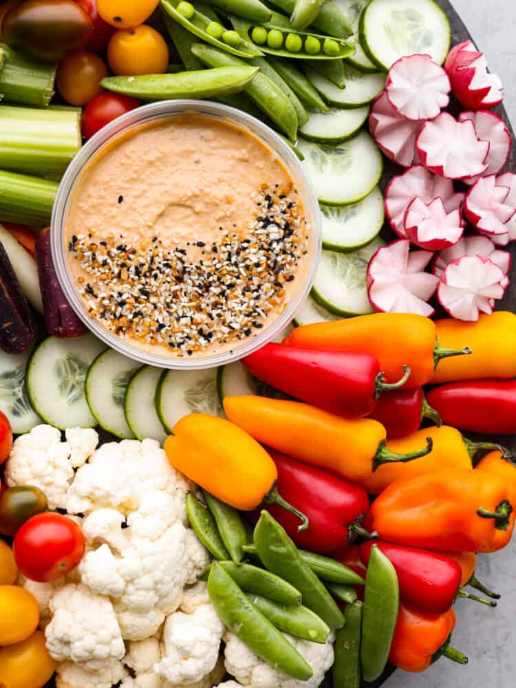 Top view of hummus surrounded by lots of veggies.  Bagel seasoning is sprinkled on top of the hummus.