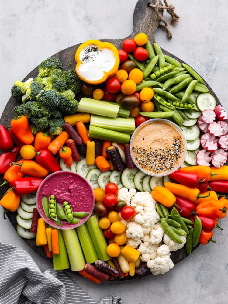 Top view of a veggie charcuterie board on a large round wood board. A kitchen towel is styled next to it.