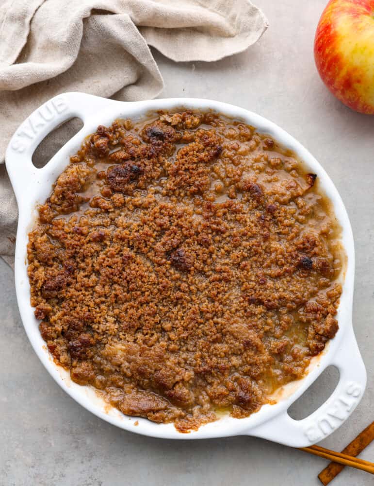 A finished and whole Apple Brown Betty in a white baking dish with a tan tea towel next to it.