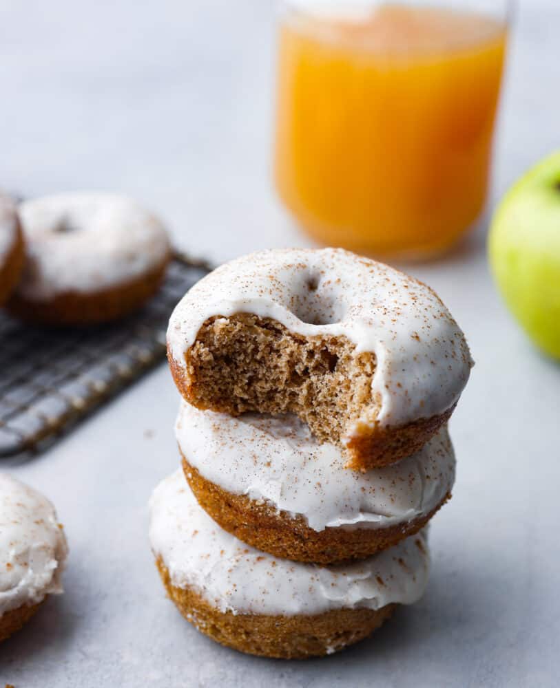 A stack of 3 donuts. The top donut has a bite taken out of it. 