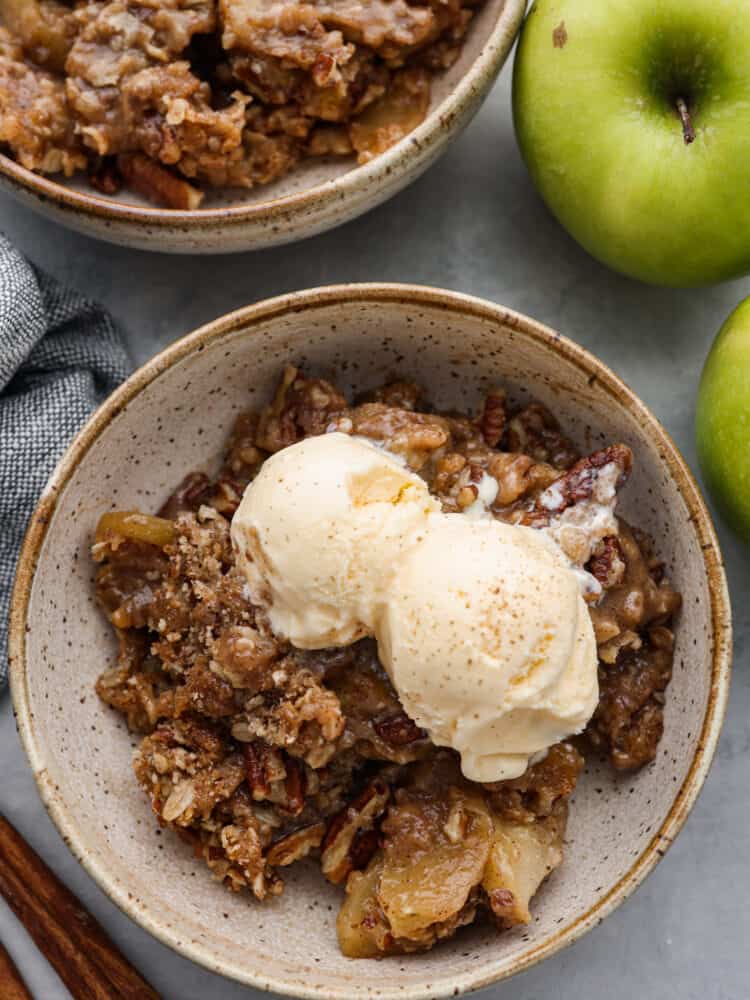 A bowl of apple pecan crisp with 2 scoops of vanilla ice cream on top,. 