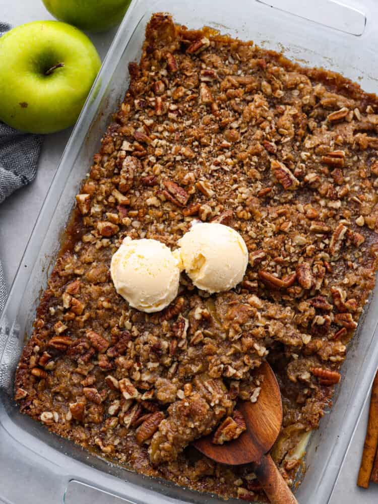 A top view of apple pecan crisp in a 9 x 13 pan with 2 scoops of vanilla ice cream on top.