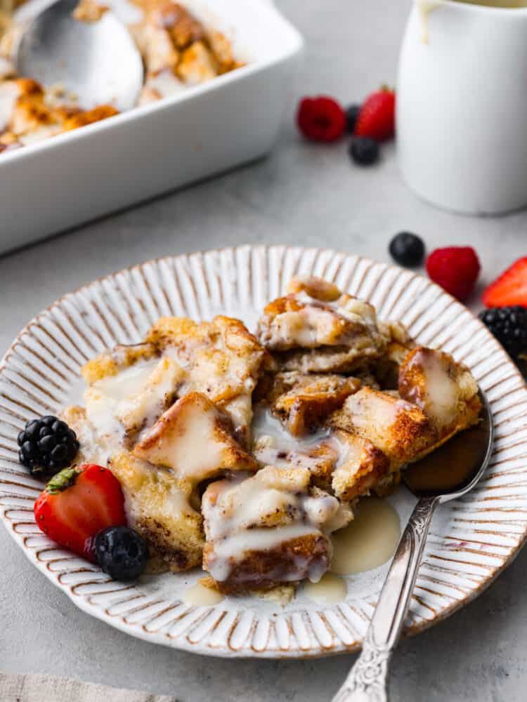 Bread pudding on a plate with fresh strawberries and blackberries and blueberries and a metal spoon.