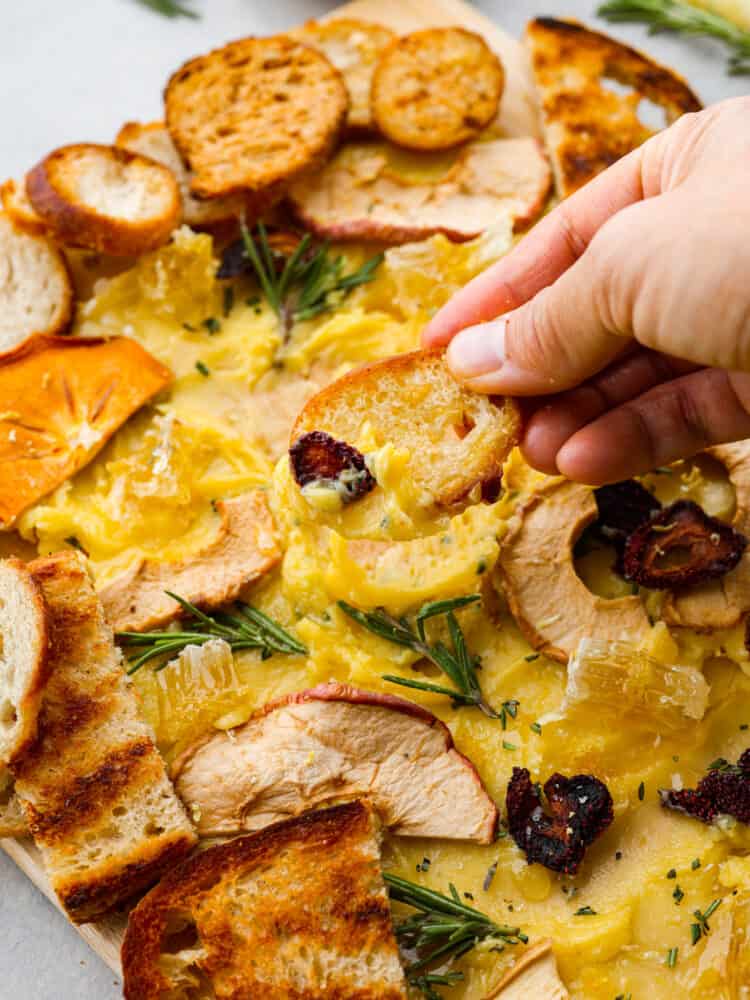 A hand scooping some butter onto a slice of crostini bread. 