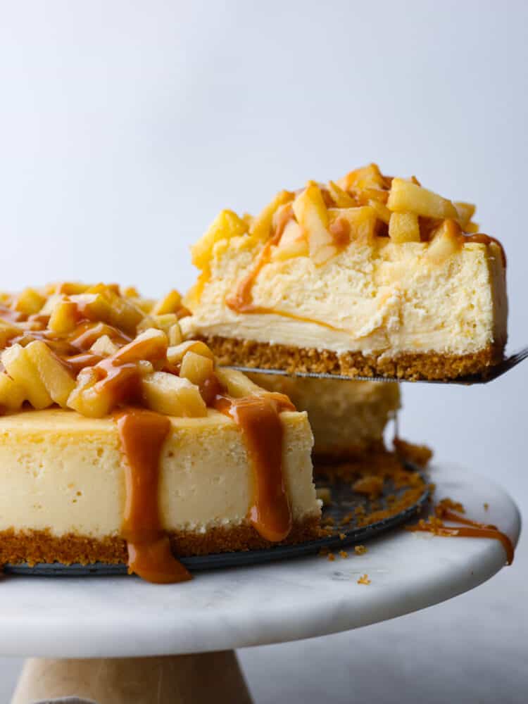 A side view of Caramel Apple Cheesecake. A slice being lifted out by a spatula.