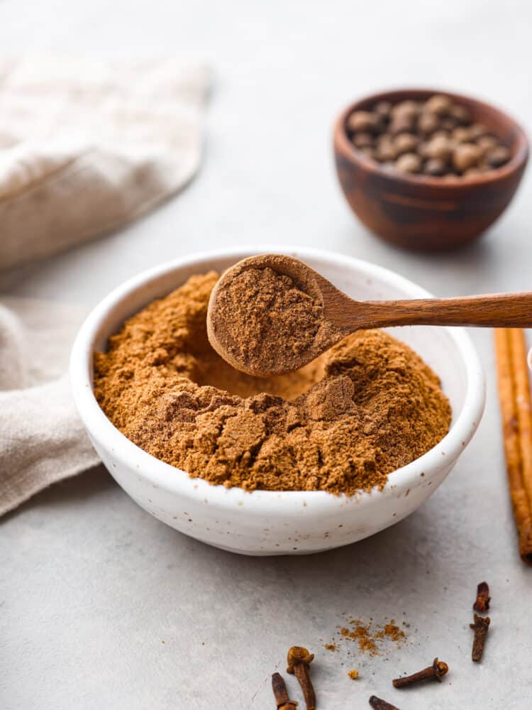 Chai Spice in a bowl with a wooden spoon that has taken a spoon full with spices in the foreground and background.