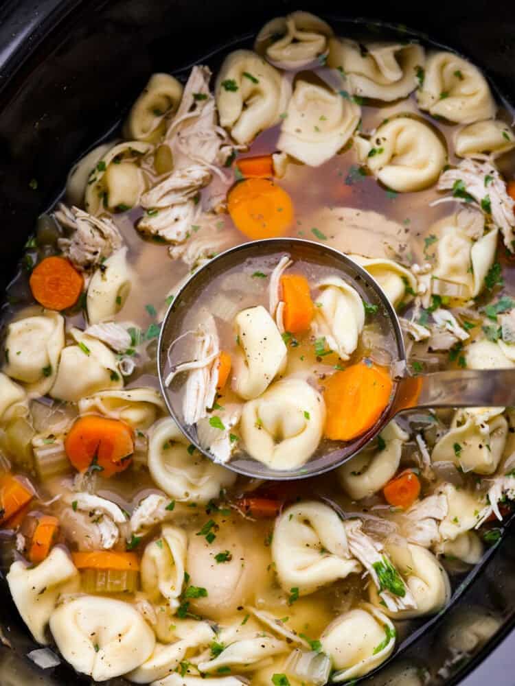 A closeup of chicken tortellini soup being scooped out of a crockpot with a ladle.