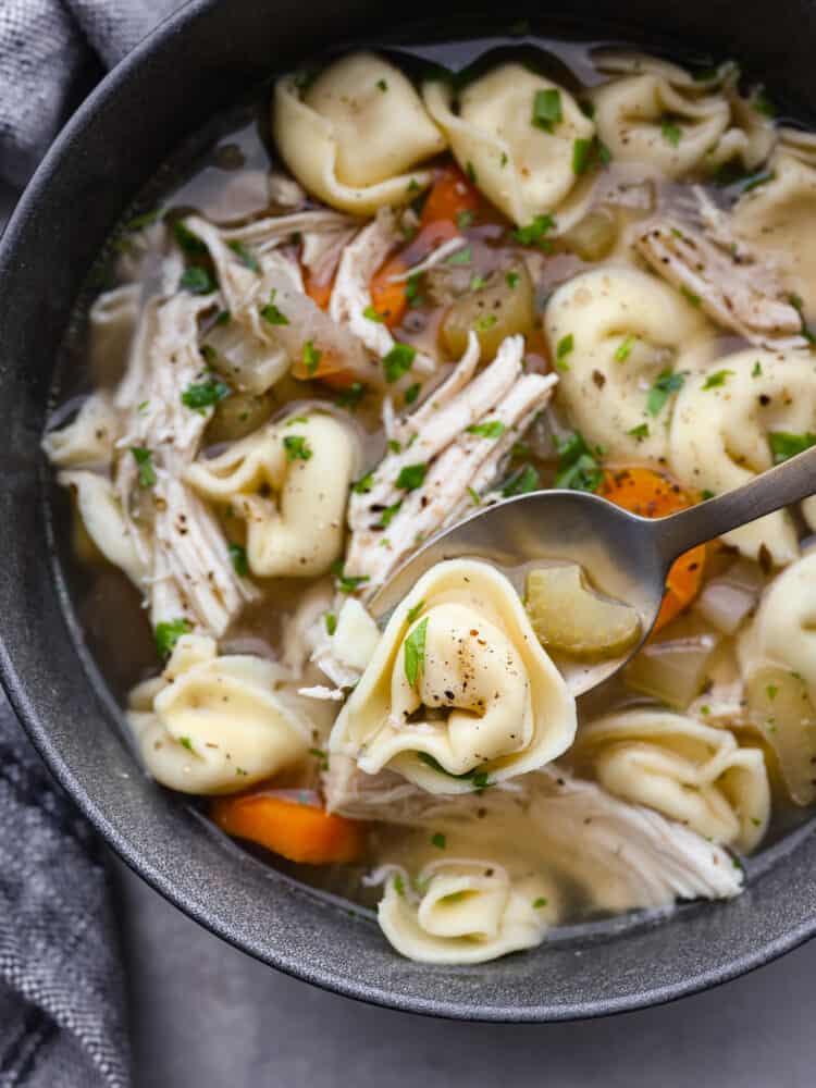 A silver spoon scooping out chicken tortellini soup from a bowl. 