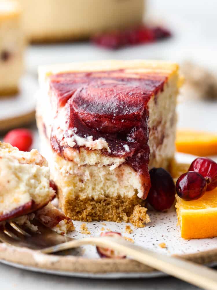 A slice of cheesecake with a bite taken out of it with a fork and fresh fruit next to it.