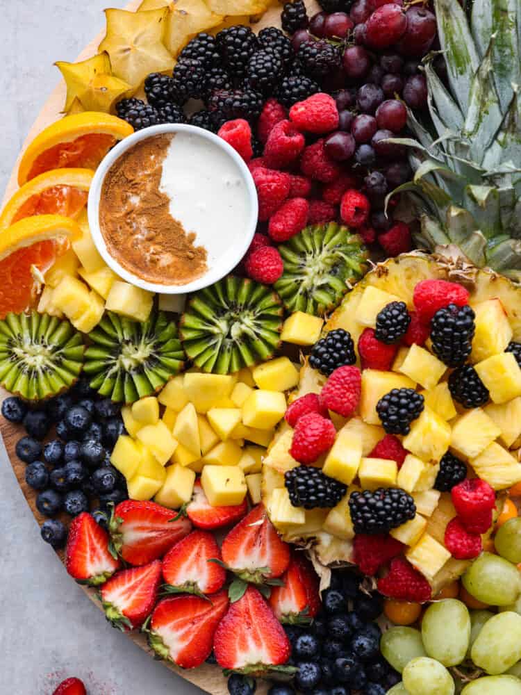 Close overhead view of the kiwi, pineapple, berries, starfruit, orange slices, and fruit dip on the charcuterie board. 