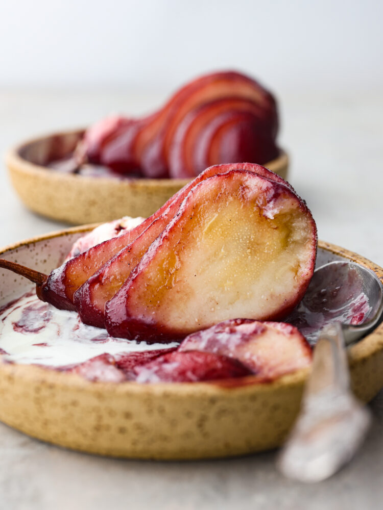 Poached pears sliced on a plate with a spoon and ice cream next to it.