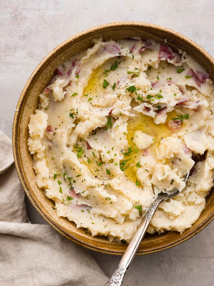 Mashed potatoes served in a brown bowl. There is a silver spoon in the bowl of potatoes.