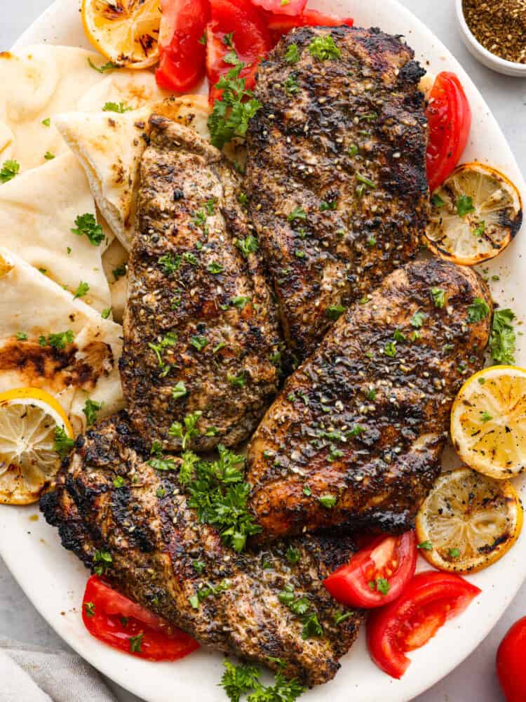 Grilled chicken on a plate with pita bread, lemons,  and tomatoes.