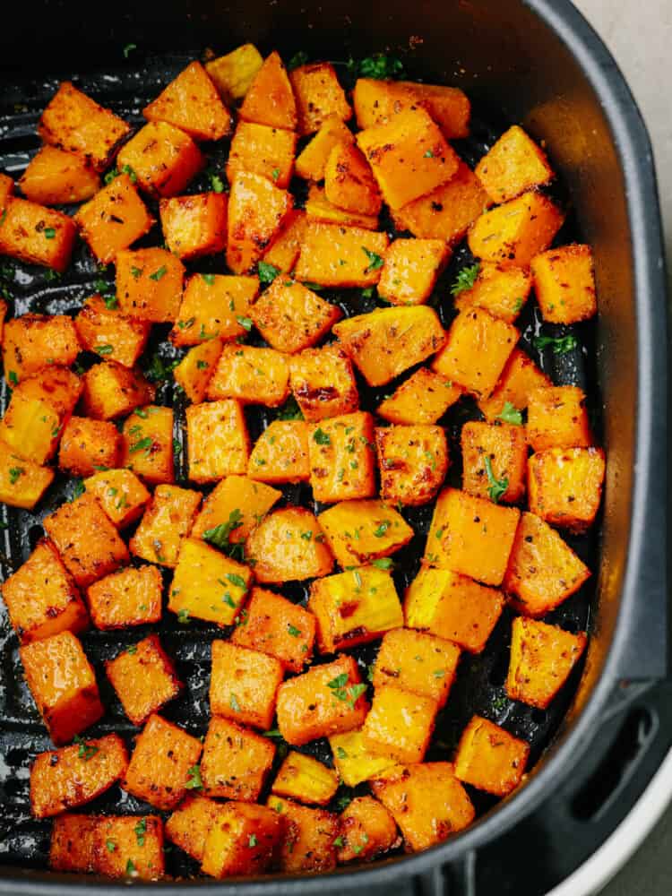 Top view of butternut squash in the air fryer and garnished with fresh chopped parsley.