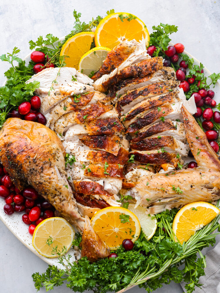 Sliced meat styled on a platter with herbs, citrus, and cranberries.