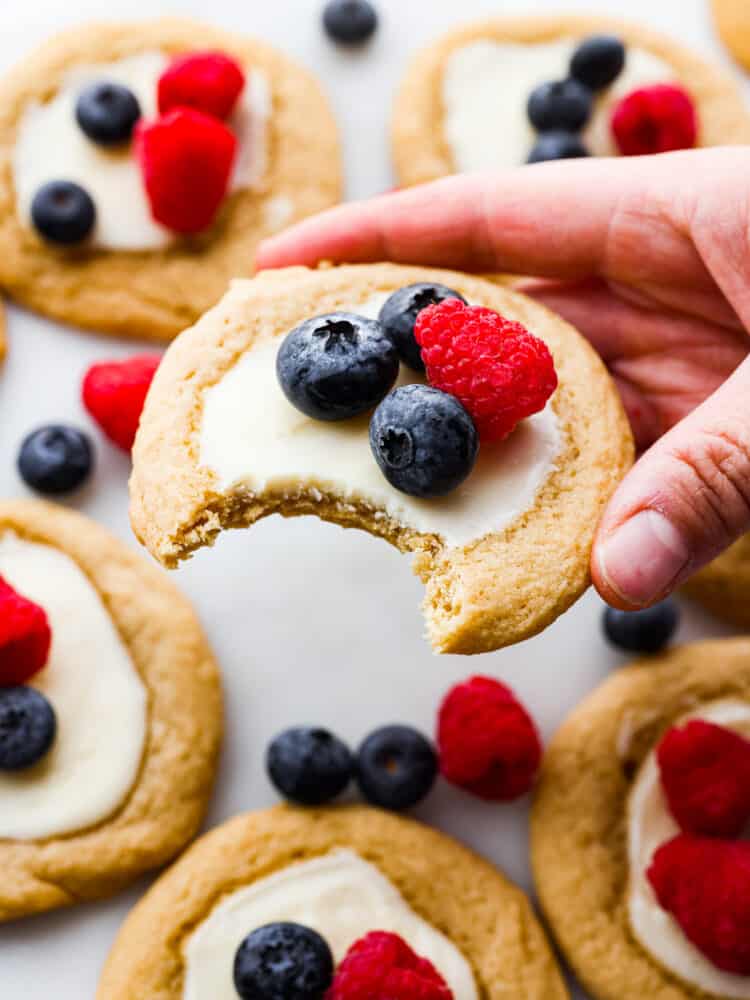 A hand holding a cookie with a bite taken out of it. 