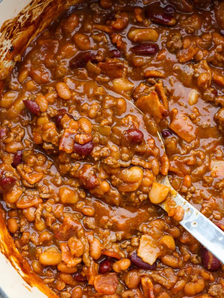 Closeup of cowboy beans being scooped with a large serving spoon.