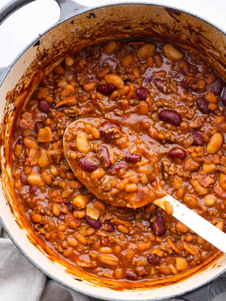 Hero image of cowboy beans in a blue and white pot. A white serving spoon is scooping some up.