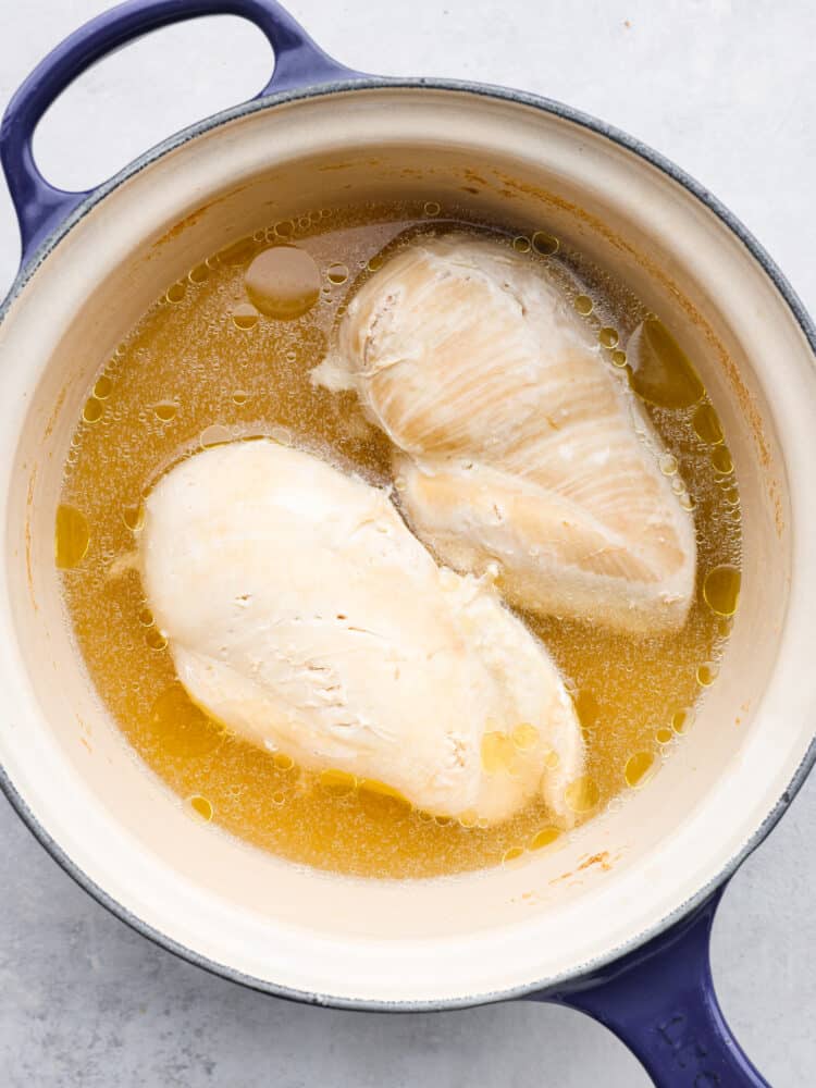 Overhead view of cooked and boiled chicken in a large blue and cream colored pot.