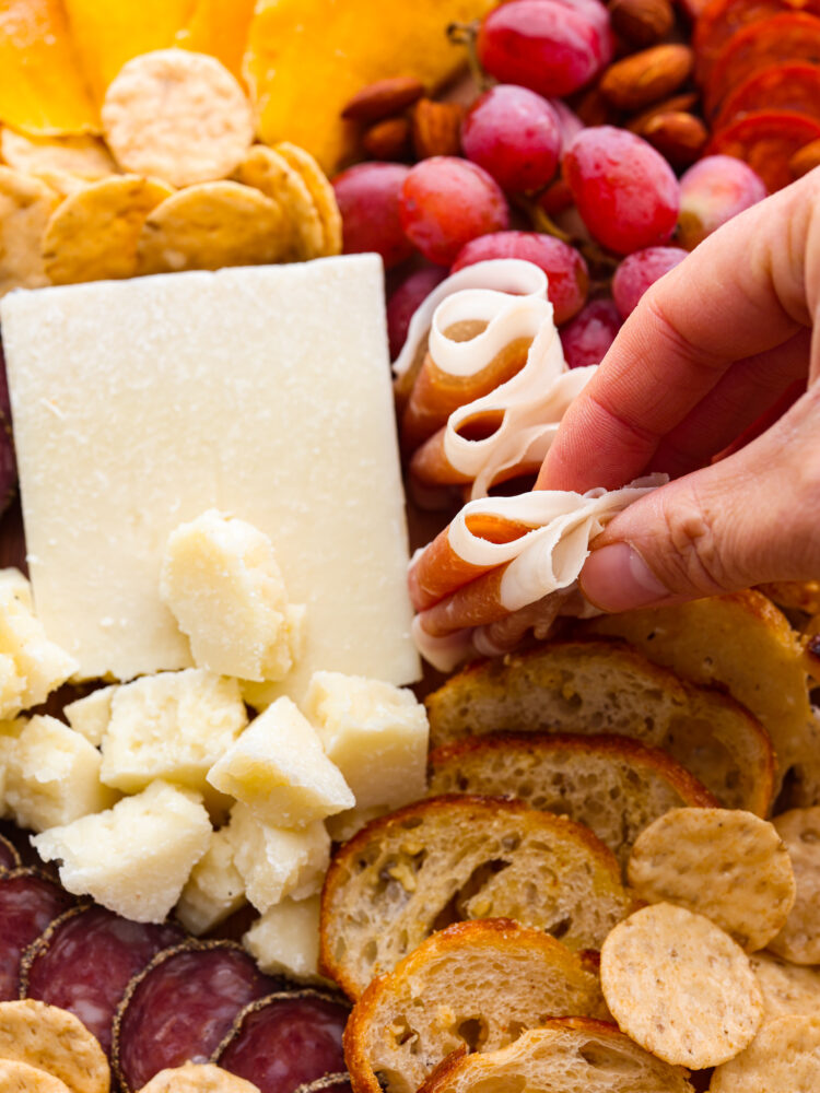 A hand grabbing some meat from the charcuterie board.