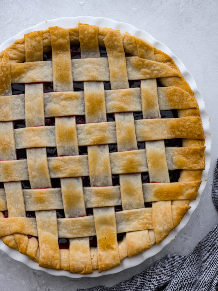 Lattice pie crust baked on top of a pie in a white dish.