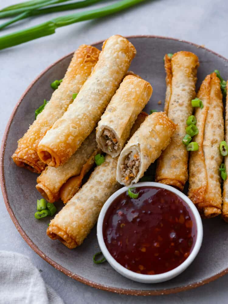 Top view of lumpia on a gray plate with a side of dipping sauce. Chopped green onion on top for garnish.